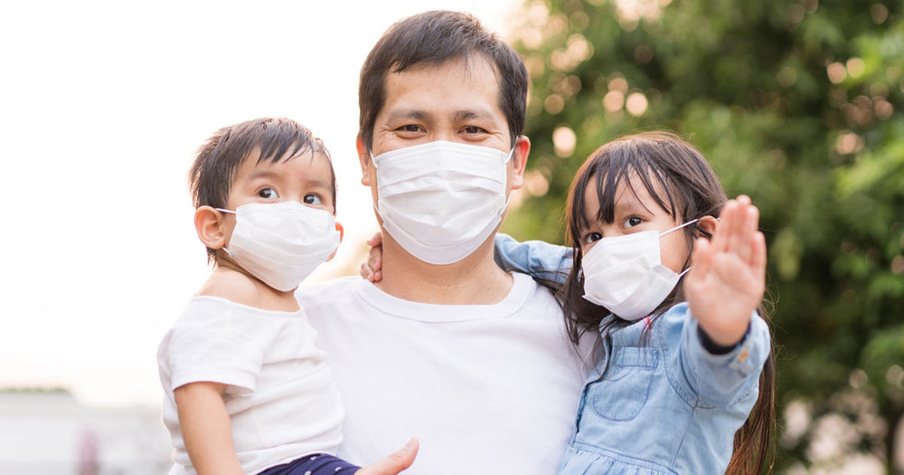 Masked father holding masked children.