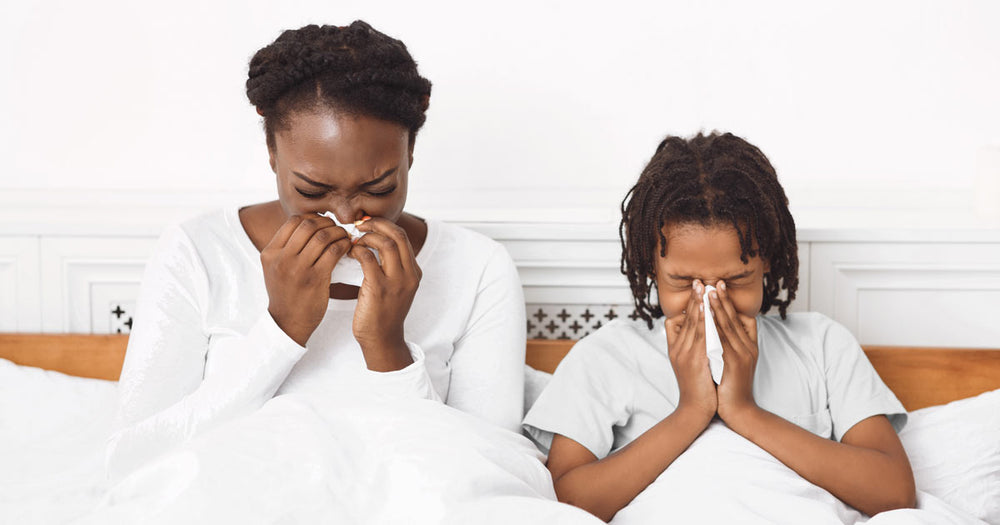 Mother and daughter in bed blowing their noses