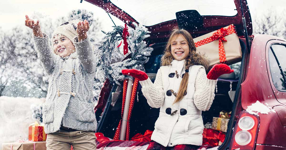 Two pre-teen girls enjoying the snowfall while sitting outside by their car