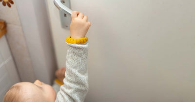 A toddler reaching up to pull down a doorhandle