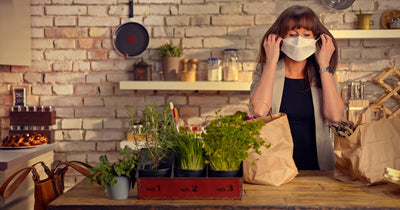 A woman at her kitchen counter removing her COVID mask after brining in her shopping