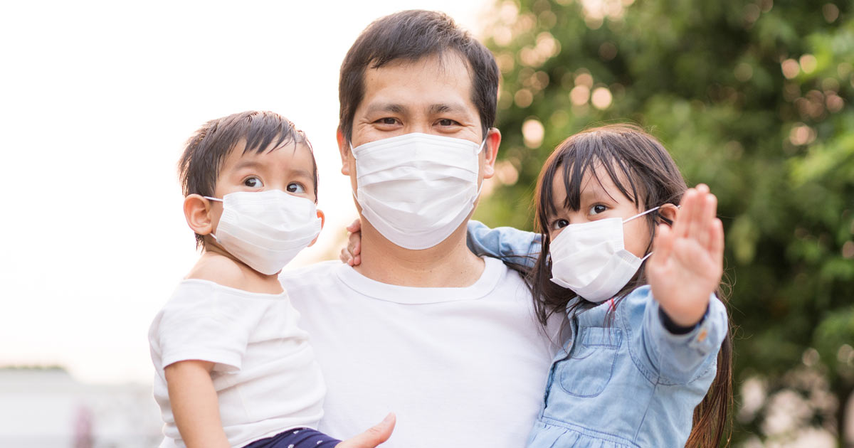 Masked father holding masked children.