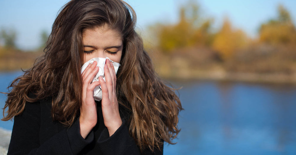 Woman blowing her nose standing outside by a lake in autumn
