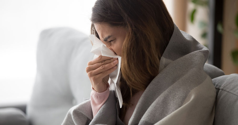 Woman suffering from hay fever sitting on her couch blowing her nose